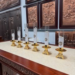 Six gold-gilded Catholic oil lamp candlesticks with glass windshields arranged on a table.