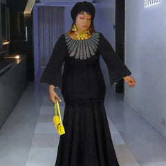 A woman wears a black long-sleeved lace maxi dress with a silver embellished neckline.