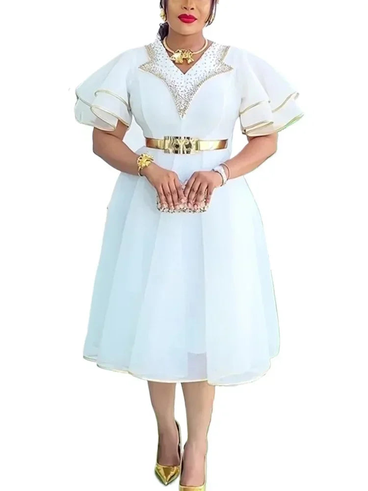 A woman wears a white midi dress with gold trim, a metallic belt, and embellished neckline.