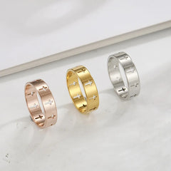 Three stainless steel rings in rose gold, gold, and silver tones featuring cutout cross patterns.