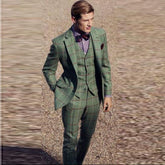A man wears a green three-piece suit with a brown windowpane check pattern and a bow tie.