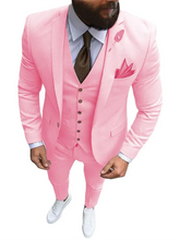 A man wears a slim-fit pink three-piece suit with a white shirt, brown tie, and white sneakers.