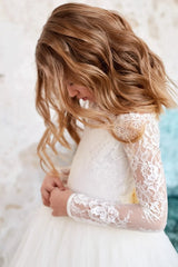 A girl wears an ivory white floor-length dress with long lace sleeves and a tulle skirt.