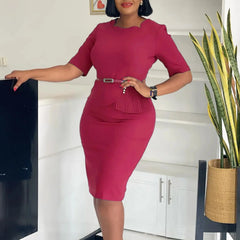 A woman wears a solid burgundy midi-length sheath dress with a square neckline and a waist belt.