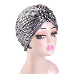 A silver pleated turban headscarf decorated with a cluster of dark beads on a mannequin head.