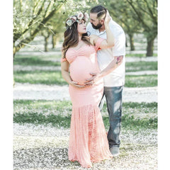 A pregnant woman wears a peach-colored, off-the-shoulder lace mermaid maternity dress.