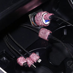 A car charger and charging cables decorated with pink rhinestones plugged into a vehicle console.