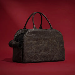 A dark brown, textured leather pet carrier bag with black handles against a red background.