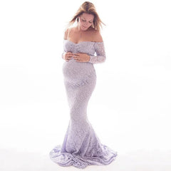 A pregnant woman wears a long-sleeved, off-the-shoulder lavender lace mermaid maternity gown.