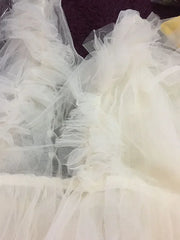 A close-up view of a champagne-colored maternity dress featuring layered tulle ruffles.