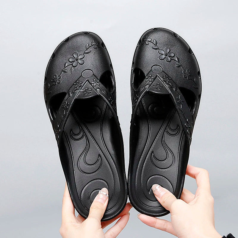 A pair of black women's slip-on sandals featuring floral cutouts and a textured footbed.