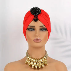 A red pleated turban headscarf featuring a black beaded floral embellishment on the front.