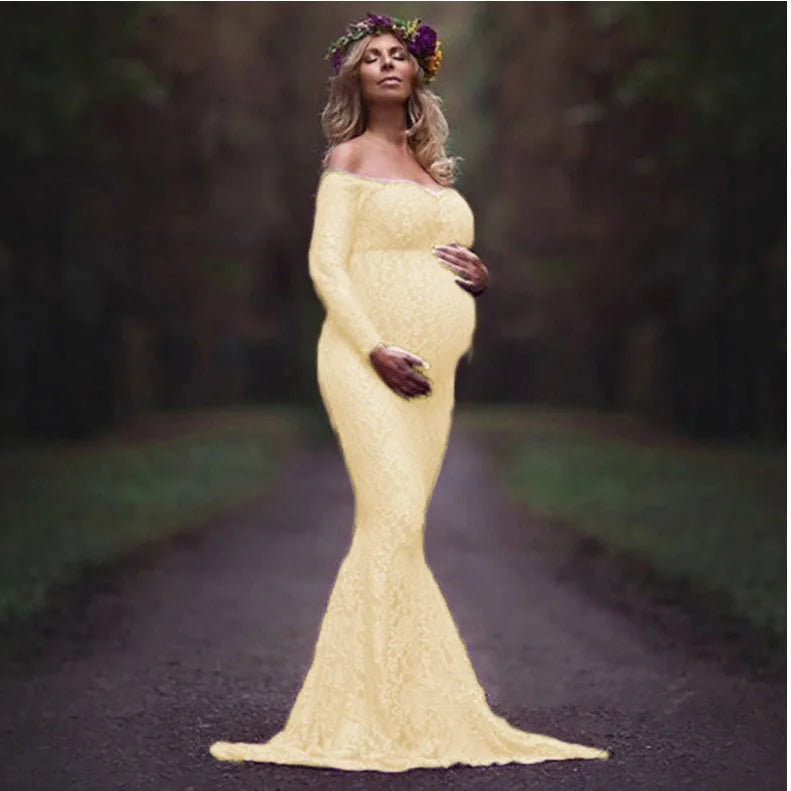 A pregnant woman wears a long-sleeved, off-shoulder cream lace mermaid maternity gown.