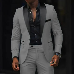 A man wears a slim-fit grey two-piece suit featuring a black shawl lapel and a black button-up shirt.