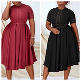 Two women model a short-sleeved, pleated A-line dress with contrast stitching in red and black.