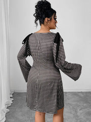 A woman wears a black and white gingham knee-length dress with long sleeves and shoulder ties.