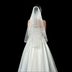 A two-layer shoulder-length white wedding veil with a ribbon edge and a comb.
