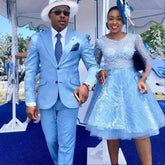 A man wearing a sky blue two-button suit with a white hat and sunglasses stands next to a woman.