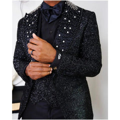 A man wears a black three-piece suit featuring a beaded, diamond-embellished peaked lapel blazer.