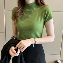A woman wears a slim-fit, short-sleeved green knitted turtleneck top with a black skirt.
