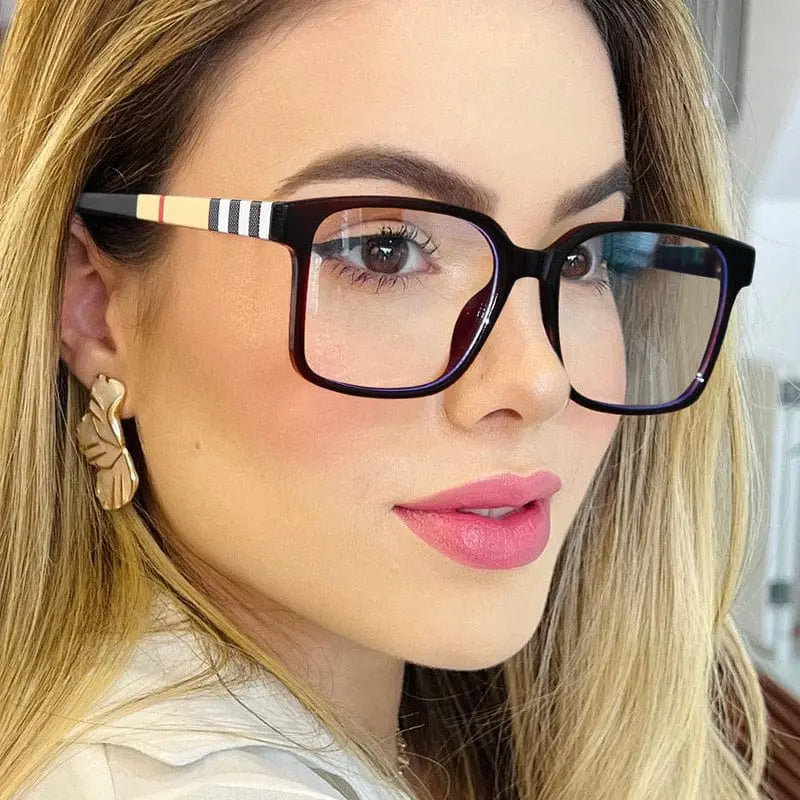 A woman with long blonde hair wears TR90 Retro Square Anti Blue Light Optical Glasses Frames with striped arms, gold statement earrings, and pink lipstick, looking slightly to the side in a well-lit indoor setting.