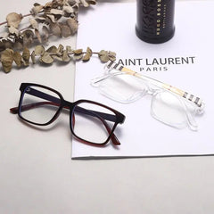 Two pairs of TR90 Retro Square Anti Blue Light Optical Glasses Frames for men and women, one black and one clear, are placed on a white paper with dried leaves and a black bottle in the background.