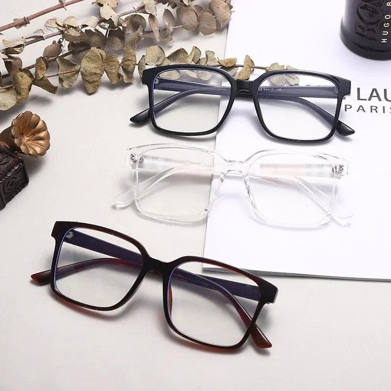 Three pairs of TR90 Retro Square Anti Blue Light Optical Glasses Frames in black, clear, and dark brown are arranged on a surface with dried leaves. Styles include cat eye and metal frames, ideal for office or computer use.