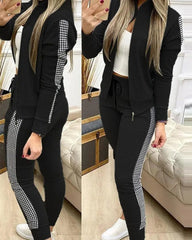 A woman wears a black two-piece tracksuit featuring a zip-up jacket and leggings with checkered side stripes.