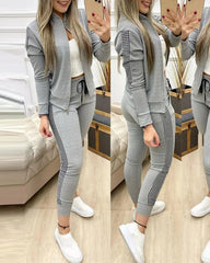 A woman wears a grey two-piece tracksuit featuring a zippered stand-collar jacket and leggings with black and white checkered side stripes.