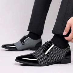 Someone wearing Trending Classic Men Dress Shoes For Men Oxfords—black patent leather lace-up shoes with a glossy, patterned finish—paired with black socks and dark trousers, adjusts their right shoe.
