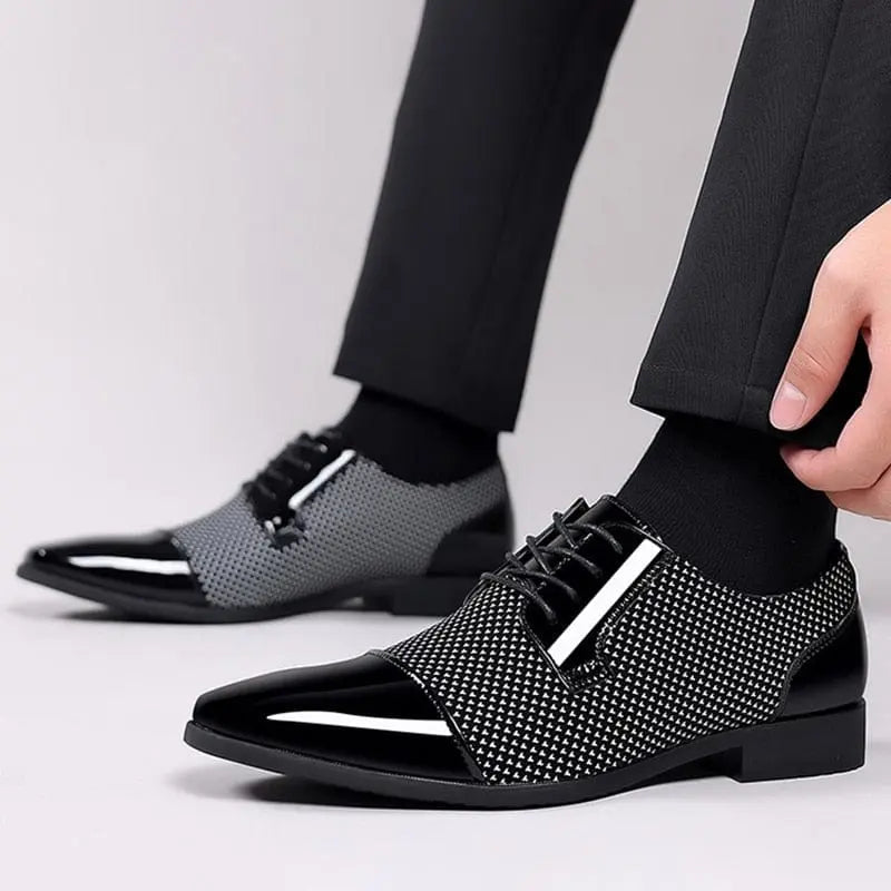 A person in black dress pants adjusts the laces of Trending Classic Men Dress Shoes—formal black patent leather Oxfords with a glossy finish and textured pattern. The background is plain and light-colored.