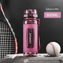 A pink Uzspace sports water bottle with a textured grip sits on a surface next to a tennis racket and baseball.