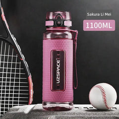 A pink Uzspace sports water bottle with a textured grip sits next to a tennis racket and baseball.