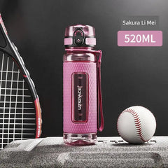 A pink Uzspace sports water bottle with a textured grip sits on a grey surface next to a baseball.