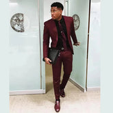 A man wears a slim-fit burgundy two-piece suit with a black shirt and matching loafers.