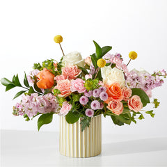 A colorful floral arrangement featuring roses and billy balls in a ribbed ivory vase.