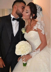 A bride wears a long-sleeved, floor-length ball gown wedding dress with lace appliques and beading.