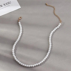 The Vintage Style Simple 6MM Pearl Chain Choker Necklace for women, featuring simulated pearls and a gold chain extender, is displayed on a light gray surface beside a partially visible white card.