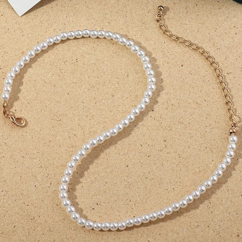 The Vintage Style Simple 6MM Pearl Chain Choker Necklace features pearls and a shell pendant on a gold chain, arranged elegantly on a beige surface—an ideal addition to any women's fashion jewelry collection.