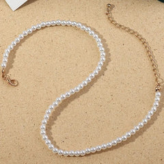 The Vintage Style Simple 6MM Pearl Chain Choker Necklace features pearls and a shell pendant on a gold chain, arranged elegantly on a beige surface—an ideal addition to any women's fashion jewelry collection.