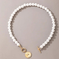The Vintage Style Simple 6MM Pearl Chain Choker Necklace features simulated pearls, a gold toggle clasp, and a round shell pendant, displayed on a neutral gray background. Perfect for weddings or everyday fashion.
