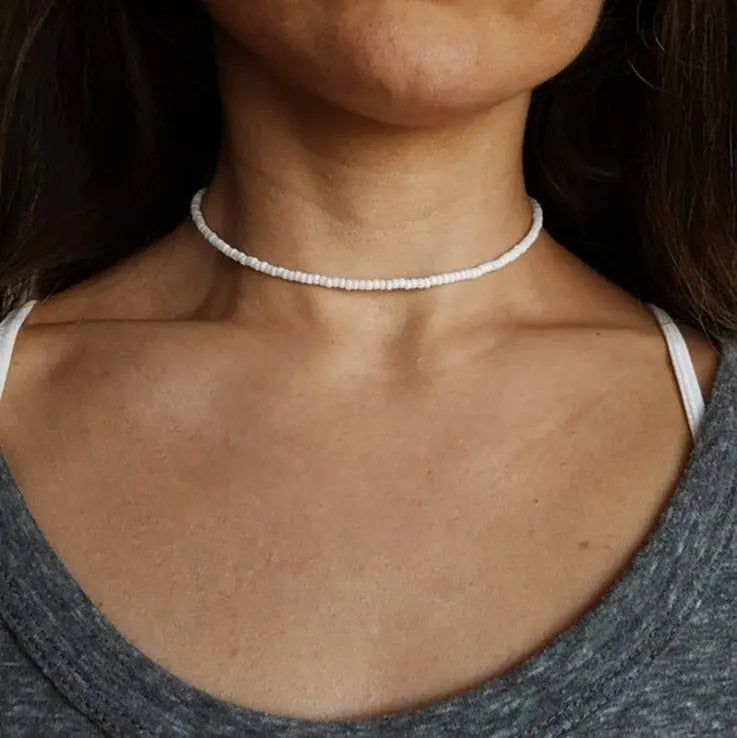 A woman wears the Vintage Style Simple 6MM Pearl Chain Choker Necklace—a white simulated pearl choker—over a gray top with a white strap showing on one shoulder.