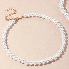 The Vintage Style Simple 6MM Pearl Chain Choker Necklace for Women features white pearls, a gold chain extender, and a shell pendant, arranged in a circle on a beige surface—perfect for weddings and fashion jewelry.