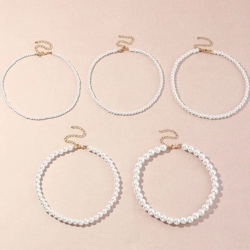 Five Vintage Style Simple 6MM Pearl Chain Choker Necklaces for women, each with gold clasps and assorted bead patterns, are displayed on a light pink surface.