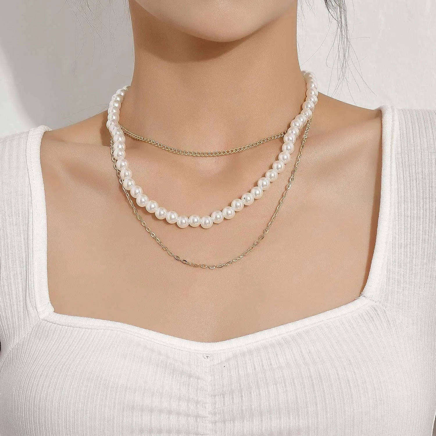 A woman in a white ribbed top wears the Vintage Style Simple 6MM Pearl Chain Choker Necklace, layered with gold chains, showcasing chic women's fashion jewelry.