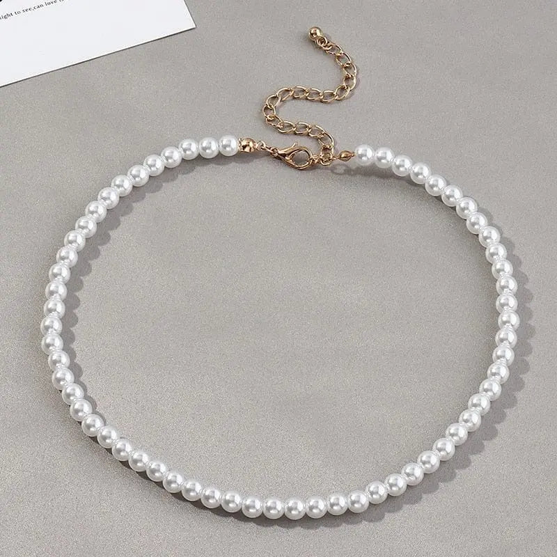 The Vintage Style Simple 6MM Pearl Chain Choker Necklace for Women, featuring evenly sized white pearls and a gold adjustable chain, is displayed on a gray surface.