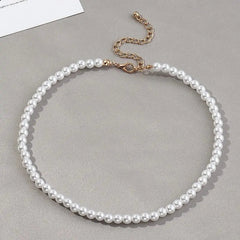The Vintage Style Simple 6MM Pearl Chain Choker Necklace for Women, featuring evenly sized white pearls and a gold adjustable chain, is displayed on a gray surface.