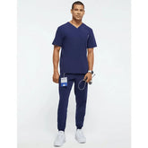 A man wearing a navy blue V-neck scrub top and matching jogger pants.