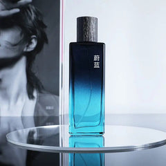 A blue gradient bottle of Wholesale Perfume Scents Long Lasting Fragrances Men Cologne rests on a reflective surface with Chinese characters on it and a black-and-white photo of a person in the background.