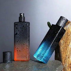Two rectangular bottles of Wholesale Perfume Scents Long Lasting Fragrances Men Cologne—one orange-to-black upright without its cap, one blue-to-black leaning on a rock. Both are covered in water droplets for a refreshing effect.